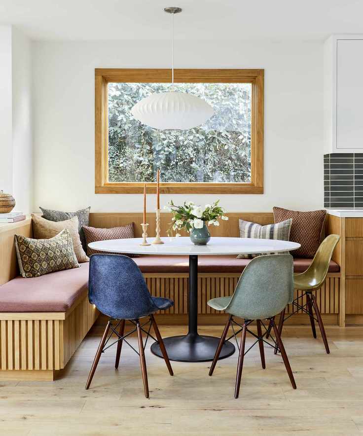 A small dining room idea with a white oak dining bench and colored chairs with white walls