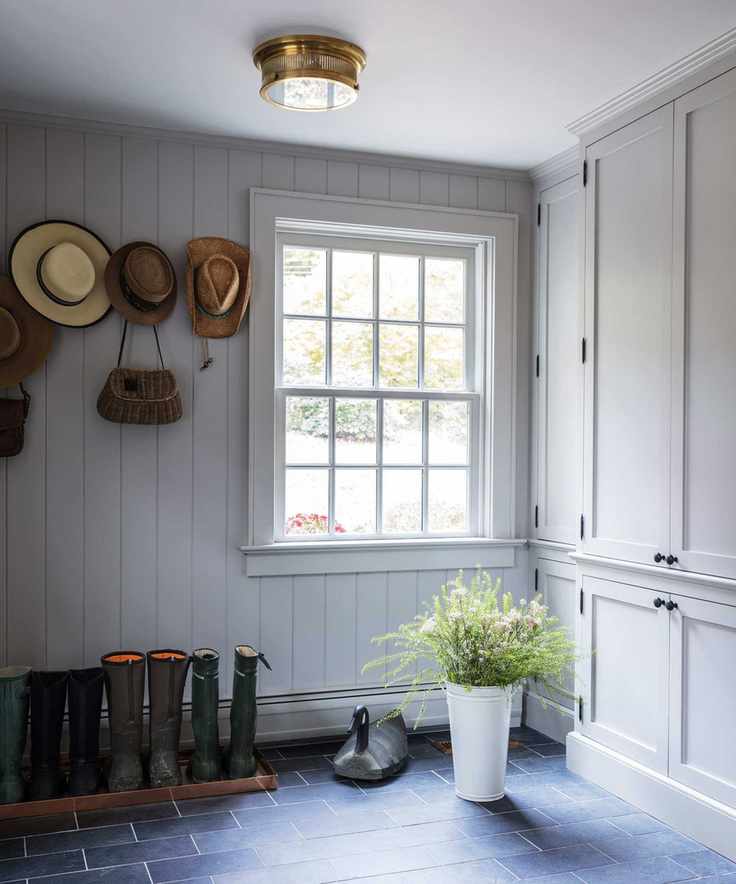 A simple mudroom with wellies stored on the floor, hats stored on coat pegs and a large window