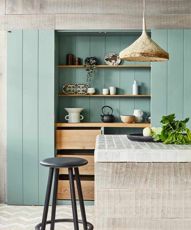 A neutral kitchen island in front of green kitchen wall panels and a hidden storage space