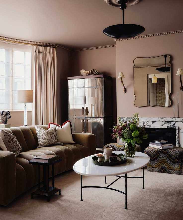 dark moody dusty pink color drench living room with a dark olive velvet sofa, marble fireplace, and a mirrored cabinet