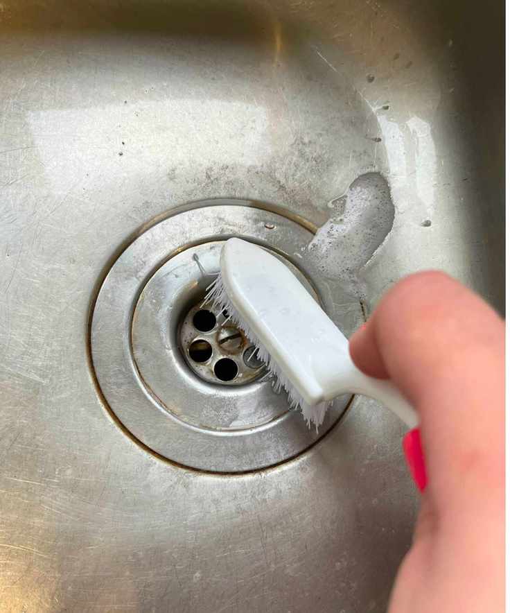 Close up of stainless steel sink drain with tea and coffee stains being cleaned by a scrubbing brush